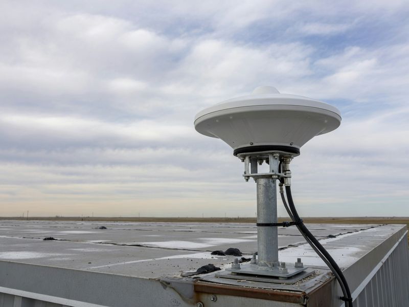 GNSS antenna on a roof mast above open country.